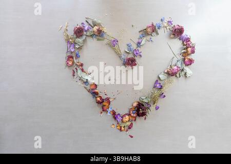 Getrocknete Blüten aus verschiedenen Blüten in Kombination mit frischen Blüten bilden ein farbenfrohes Blumenarrangement in Form eines Blumenherzes Stockfoto