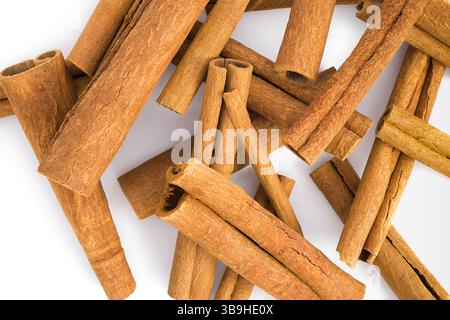 Nahaufnahme von gebrochenen Zimtrindenstücken auf einer weißen Oberfläche, die ihre rustikale Textur, Erdfarben und natürliche Mängel zeigen, die für Kubikprodukte geeignet sind Stockfoto