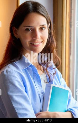 Frau, die in die Kamera schaut, mit einem Buch in den Armen Stockfoto
