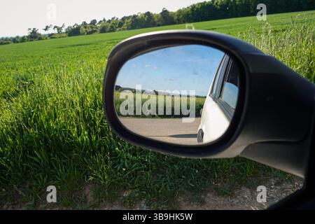 Der Rückspiegel eines Autos zeigt ein Feld mit blauem Himmel Stockfoto