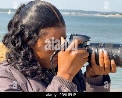 Calshot Hampshire England Vereinigtes Königreich. 27.04.2025. Afrikanerin mit DSLR-Digitalkamera bei einem Besuch am Calshot Beach in Hampshire UK Stockfoto