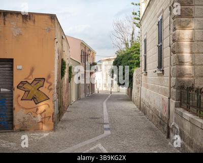 Horizontaler Weitwinkelblick auf eine kopfsteingepflasterte Straße mit Orangenfassade und Baum in Olbia Altstadt, Sardinien, Italien Stockfoto
