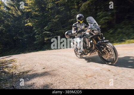 Abenteuer Motorradfahrer fahren tagsüber auf einer Schotterstraße. Der Biker trägt volle Schutzausrüstung und Helm, während er in Kurven auf einem robusten Stockfoto