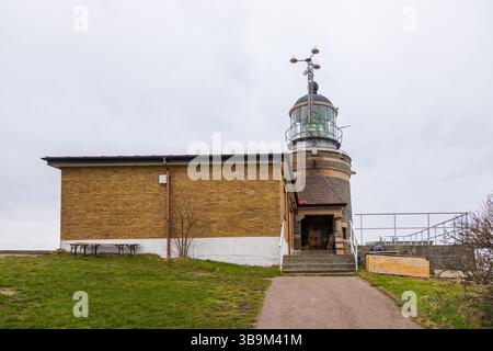 Alter Leuchtturm auf einer felsigen Klippe am Meer in Kullen, Schweden. Bewölkter Frühlingstag an der Küste. Stockfoto