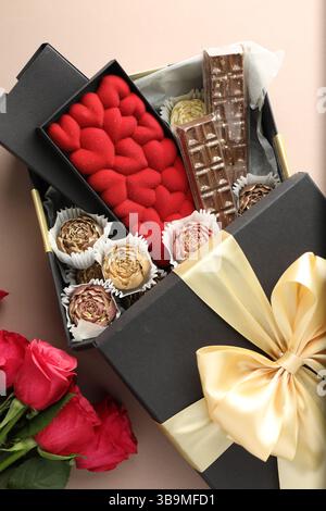 Verschiedene köstliche Schokoladenbonbons in der Box und Rosen auf beigefarbenem Hintergrund, Blick von oben Stockfoto
