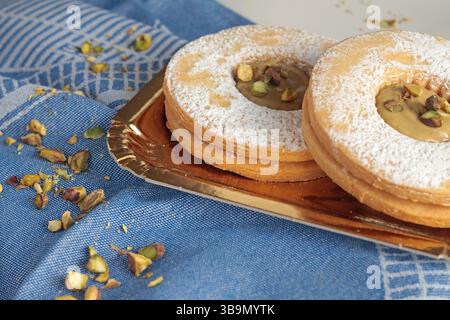 Shortbread Teiggebäck mit Pistaziencreme und Nüssen auf goldener Papierplatte. Dessert für Party, Feier. Stockfoto