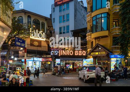 Abendliche Szene einer belebten Straße in Vietnam, mit verschiedenen beleuchteten Geschäften mit verschiedenen Ladenfronten und Schildern, die Passanten anziehen. Stockfoto