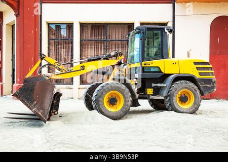 Ein gelber Planierschild mit Rädern und einem vorderen Schaufel steht in der Stadt auf einer Baustelle. Stockfoto