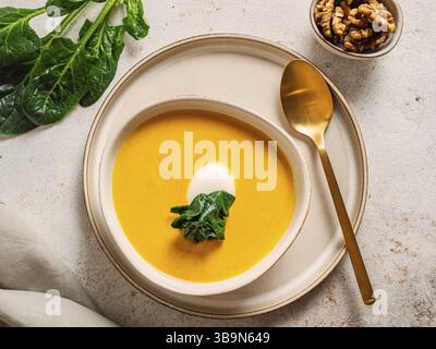 Kürbiscremesuppe serviert Spinat, Nüsse, Sauerrahm. Leckerer hausgemachter Kürbis, süße Kartoffel oder Karottensuppe in der Schüssel auf neutralem Pastelhintergrund. Gemütliches Au Stockfoto