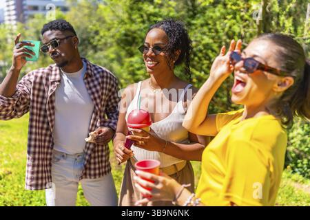 Drei Freunde haben gemeinsam Spaß in einem Park und genießen an einem sonnigen Tag erfrischende Getränke und Snacks Stockfoto