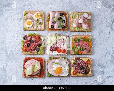 Set aus acht verschiedenen Sandwiches mit Fleisch in quadratischer Form. Draufsicht oder flaches Lay. Sortiment Fleisch Toast auf grauem Zement Hintergrund. Idee, kreativer Co Stockfoto
