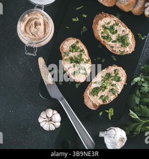 Blick von oben auf Brotscheiben mit hausgemachter putenpastete und frischer grüner Petersilie auf schwarzem kutterbrett über schwarzem Zementhintergrund Stockfoto