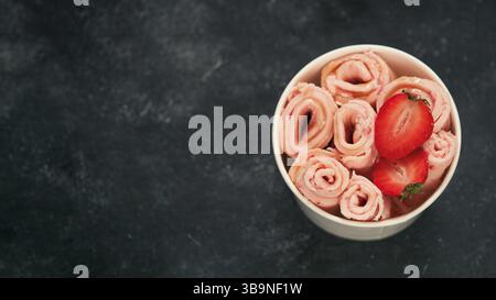 Gerolltes Eis mit Erdbeere in Kegelbecher auf dunklem Hintergrund. Erdbeer Eisrollen Draufsicht oder flach legen. Thailändisches Eiscreme mit Copy Spa Stockfoto