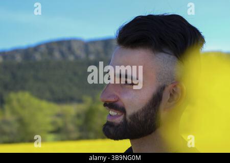 Nahporträt eines jungen bärtigen Mannes, der lächelnd zum Horizont blickt Stockfoto