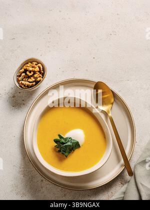 Kürbiscremesuppe serviert Spinat. Leckerer hausgemachter Kürbis, süße Kartoffel oder Karottensuppe in der Schüssel auf neutralem Pastelhintergrund. Gemütliche Herbstgerichte. Stockfoto