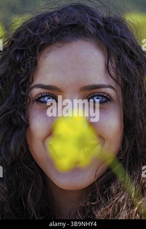 Nahporträt einer jungen blauäugigen Frau hinter einer gelben Blume Stockfoto
