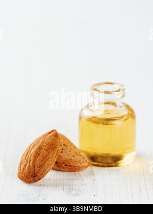 Kleines Glas Flasche Mandelöl und Mandeln auf weißem Holz der Tischplatte mit kopieren. Vertikale Stockfoto