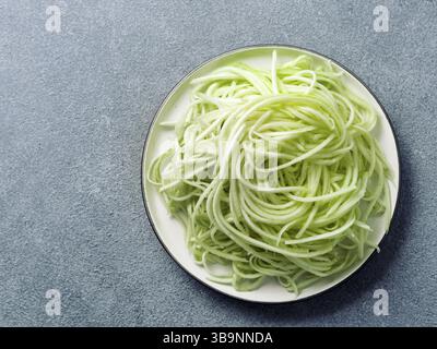 Zucchini Nudeln auf dem Teller. Gemüse Nudeln - Grün zoodles oder Zucchini Spaghetti auf die Platte über der grauen Stein Hintergrund. Sauber Essen, raw Vegetarische foo Stockfoto