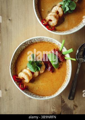 Tom Yam kong Ready-to-eat. Tom Yum Suppe mit Garnelen auf hölzernen Tisch. Beliebte würzige Thailändisches Gericht Tom Yam Ansicht von oben. Thailand Essen und thailändische Küche. Vertic Stockfoto