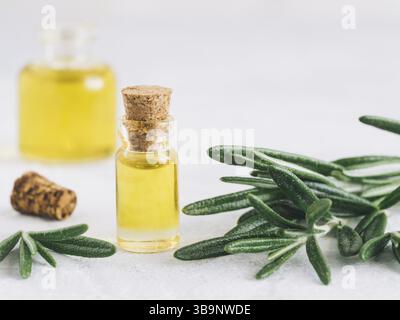 Rosmarinöl. Ätherisches Rosmarinöl in kleiner Glasflasche und Zweigen pflanzlichen frischen Rosmarins auf weißem Hintergrund. Kopierbereich für Text Stockfoto