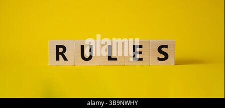 Regelsymbol. Holzwürfel mit Wort Regeln. Schöner gelber Hintergrund. Regelkonzept. Kopierbereich. Stockfoto
