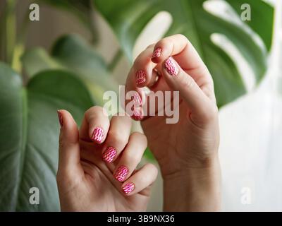 Ästhetisches Erscheinungsbild zweier weiblicher Hände mit kurzen Nägeln mit Neon-Stanzmaniküre. Hand mit stilvollem, leuchtend rosa Neon Stamping Nailart Design Maniküre Stockfoto