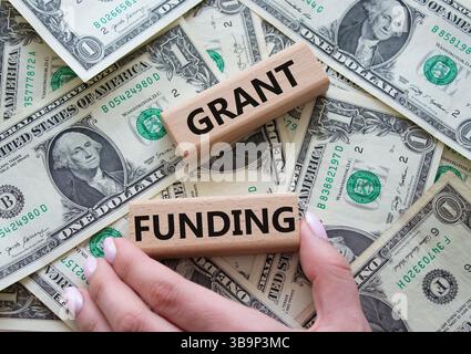 Symbol "Finanzierung gewähren". Holzblöcke mit den Worten Grant Funding. Wunderschöner Dollar-Hintergrund. Geschäftsmann Hand. Konzept für die Finanzierung von Unternehmen und Zuschüssen. Kopieren Stockfoto