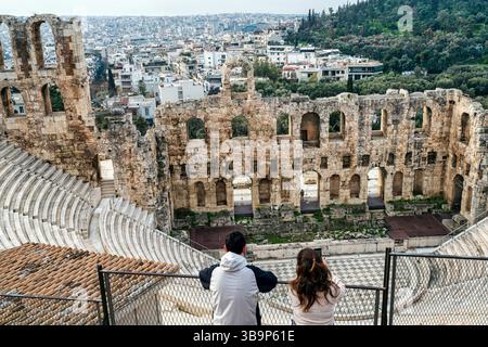 Touristen mit Blick auf das antike römische Amphitheater Odeon des Herodes Atticus auf der Akropolis mit dem dahinter liegenden Stadtbild von Athen. Stockfoto