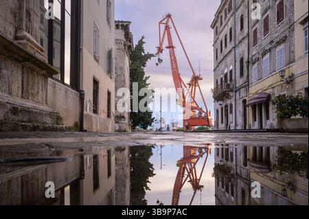 Der Kran spiegelt sich in einer Pfütze entlang der Uferstraße von Pula, Kroatien, und zeigt den industriellen Charakter des Hafens in der Dämmerung Stockfoto