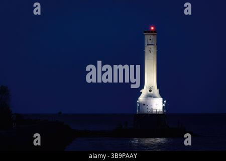 Eine eindrucksvolle Nachtszene mit einem hohen weißen Leuchtturm, der vor dem tiefblauen Himmel beleuchtet wird und entlang der Küste mit seinem roten Leuchtfeuer steht Stockfoto