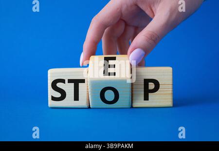Symbol „Schritt vs. Stopp“. Die Hand des Geschäftsmannes dreht Holzwürfel und ändert das Wort Stop to Step. Wunderschöner blauer Hintergrund. Schritt vs. Stopp und Business Conce Stockfoto