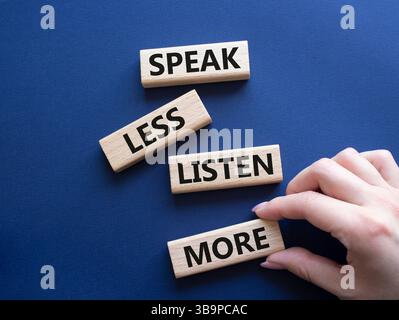 Weniger sagen, mehr hören. Holzblöcke mit Wörtern sprechen weniger Hören Sie mehr. Wunderschöner tiefblauer Hintergrund. Geschäftsmann Hand. Geschäftlich und sprechen Sie l Stockfoto