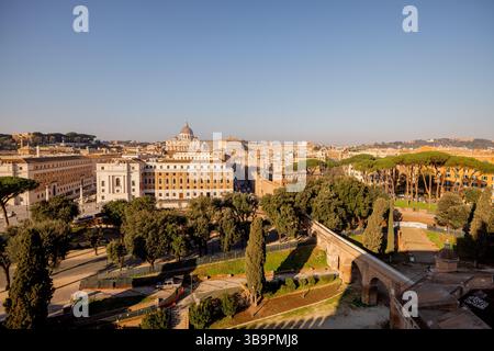 Panoramablick auf Vatikanstadt und die Kuppel des Petersdoms von der Spitze des Engelsburg, eingerahmt von römischen Kiefern und Morgensonne über den Dächern Roms Stockfoto
