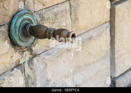 Nahaufnahme des alten Retro-Metallwasserhahns auf dem alten Steinbrunnen mit fließendem Wasser Stockfoto
