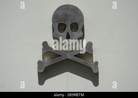 Schädel- und Kreuzknochensymbol an einer weißen Wand in Sevilla, Spanien, für ein kühnes Warnungs- und Gefahrenkonzept mit starkem Schatten. Sevilla, Spanien Stockfoto