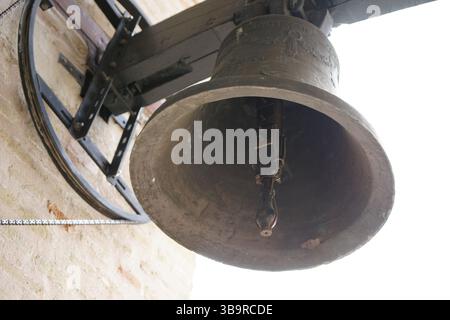 Historische Kirchenglocke hängt in einem Glockenturm in Sevilla, Spanien, fotografiert von unten mit Mauerwerk und Metallstützen. Sevilla, Spanien Stockfoto