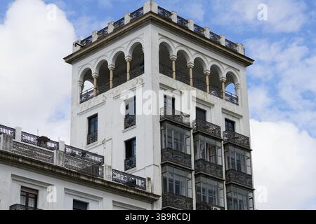 Historisches weißes Turmgebäude mit Dachbögen und schmiedeeisernen Balkonen in Sevilla, Spanien, fotografiert vor einem blauen Himmel mit Wolken. Sevilla Stockfoto