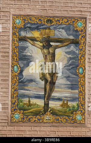 Keramikfliesen-Wandbild der Kreuzigung, die Jesus Christus am Kreuz zeigt, mit verziertem Rand an einer Ziegelmauer in Sevilla, Spanien. Sevilla, Spanien Stockfoto
