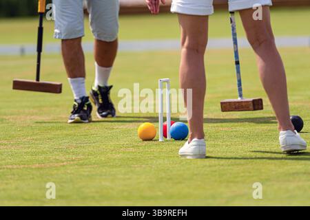 Zwei Personen spielen mittags ein lebhaftes Krocketspiel auf gut gepflegtem Gras. Stockfoto