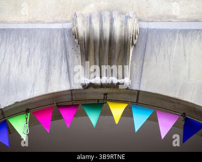 Ein dekoratives architektonisches Element über einem Bogengang mit klassischem Säulendesign. Unten, bunte dreieckige Fahnen in leuchtenden Rosa-Tönen, Stockfoto