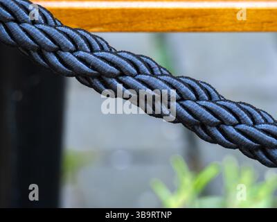 Nahaufnahme eines dicken, geflochtenen schwarzen Seils mit glatter Textur, das auf einer Holzoberfläche aufliegt. Der Hintergrund zeigt verschwommenes Grün, wodurch ein entsteht Stockfoto