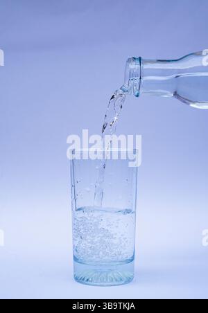 Sauberes und erfrischendes Wasser aus einer Plastikflasche in ein transparentes Glas, isoliert auf weißem Hintergrund. Das Bild stellt die Hydratation dar Stockfoto