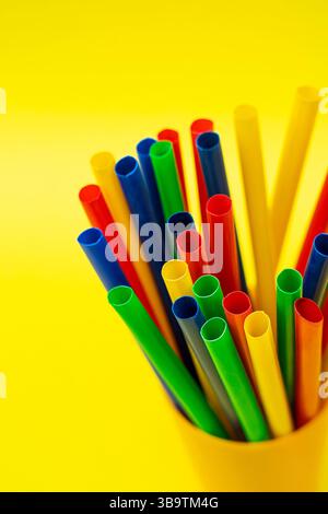 Ein Satz roter, grüner, blauer und gelber Trinkhalme, die vertikal in einem gelben Behälter platziert werden. Stockfoto