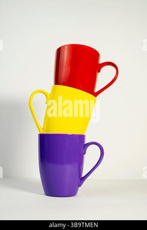 Stilvolle Keramikbecher in verschiedenen Farben, kreativ auf weißem Hintergrund angeordnet. Stockfoto