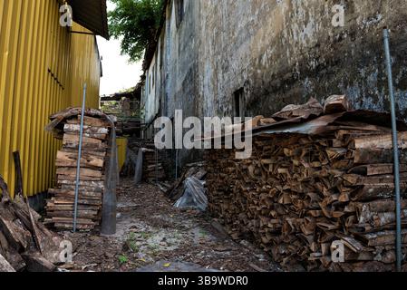 Gestapeltes Brennholz unter Metalldach im Rural Yard – sauber angeordnete Stapel aus gespaltenem Brennholz sind unter gewellten Metallblechen in einem Gras geschützt Stockfoto
