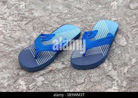 Ein Paar stilvolle marineblaue Flipflops liegt auf einem Betonboden. Dieser leichte, sandelähnliche Schuh wird normalerweise als Freizeitschuhe getragen. Stockfoto