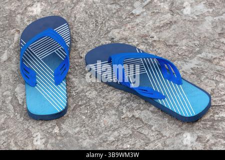 Ein Paar stilvolle marineblaue Flipflops auf einem Betonboden. Diese leichten, sandelähnlichen Schuhe werden normalerweise als Freizeitschuhe getragen. Stockfoto