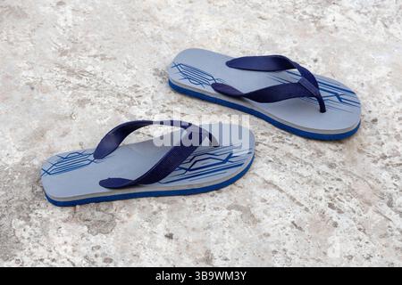 Eine stylische Flip-Flops-Sandale liegt auf einem Betonboden. Flip-Flops sind eine Art leichter, sandelähnlicher Schuh, der normalerweise als Freizeitschuhe getragen wird. Stockfoto