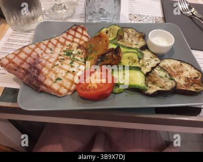 Gegrilltes Schwertfisch-Steak, serviert mit einer bunten Auswahl an gegrilltem Gemüse, einschließlich Zucchini, Auberginen und Tomaten, garniert mit Kräutern und A Stockfoto