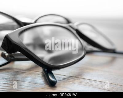 Zwei Paar schwarze Gläser liegen auf einer rustikalen Holzoberfläche. Die transparenten Gläser reflektieren weiches Licht und schaffen eine elegante Atmosphäre und einladende Fokussierung Stockfoto